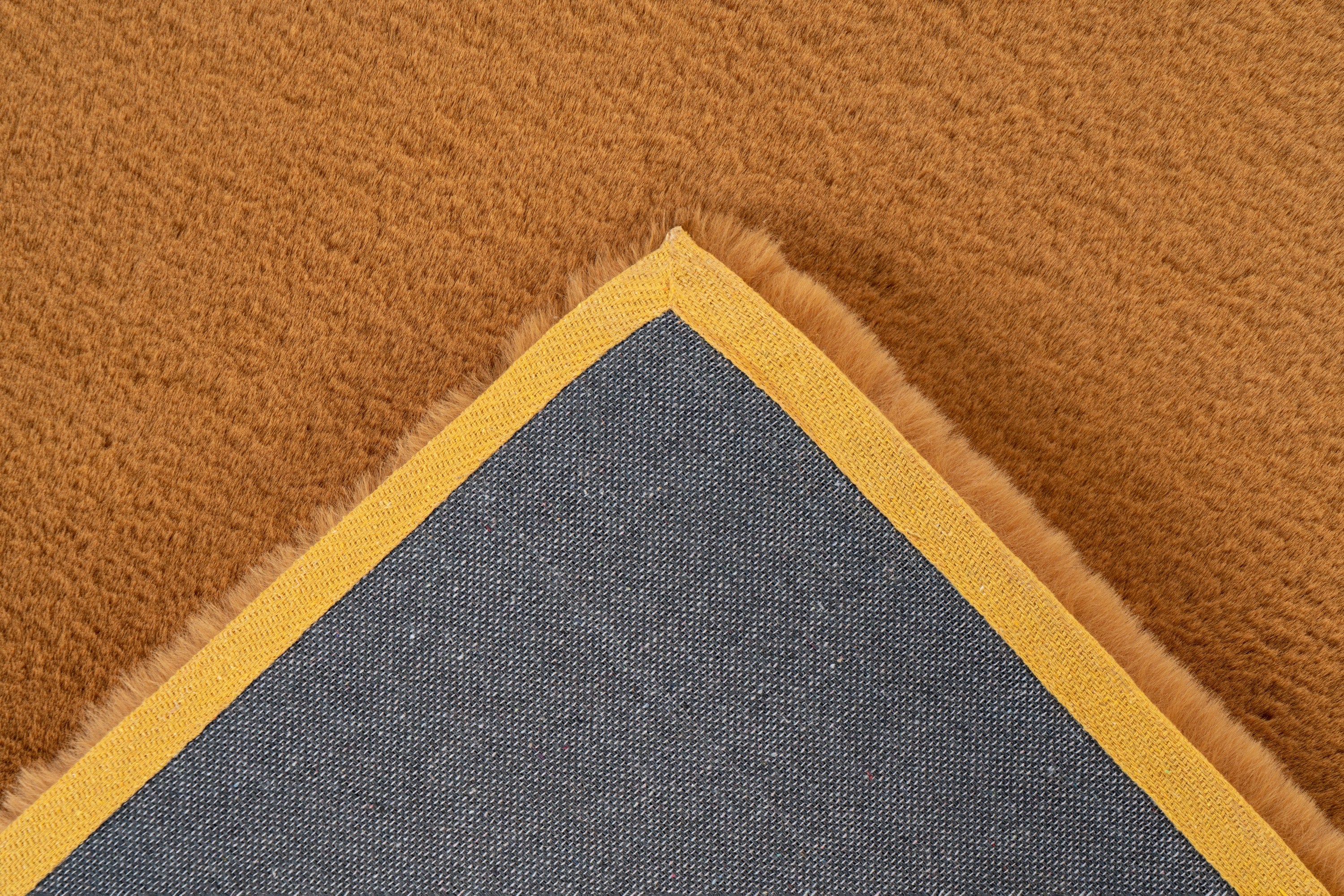Detailopname van de backing van het koperkleurige Could vloerkleed met zicht op de afwerking
