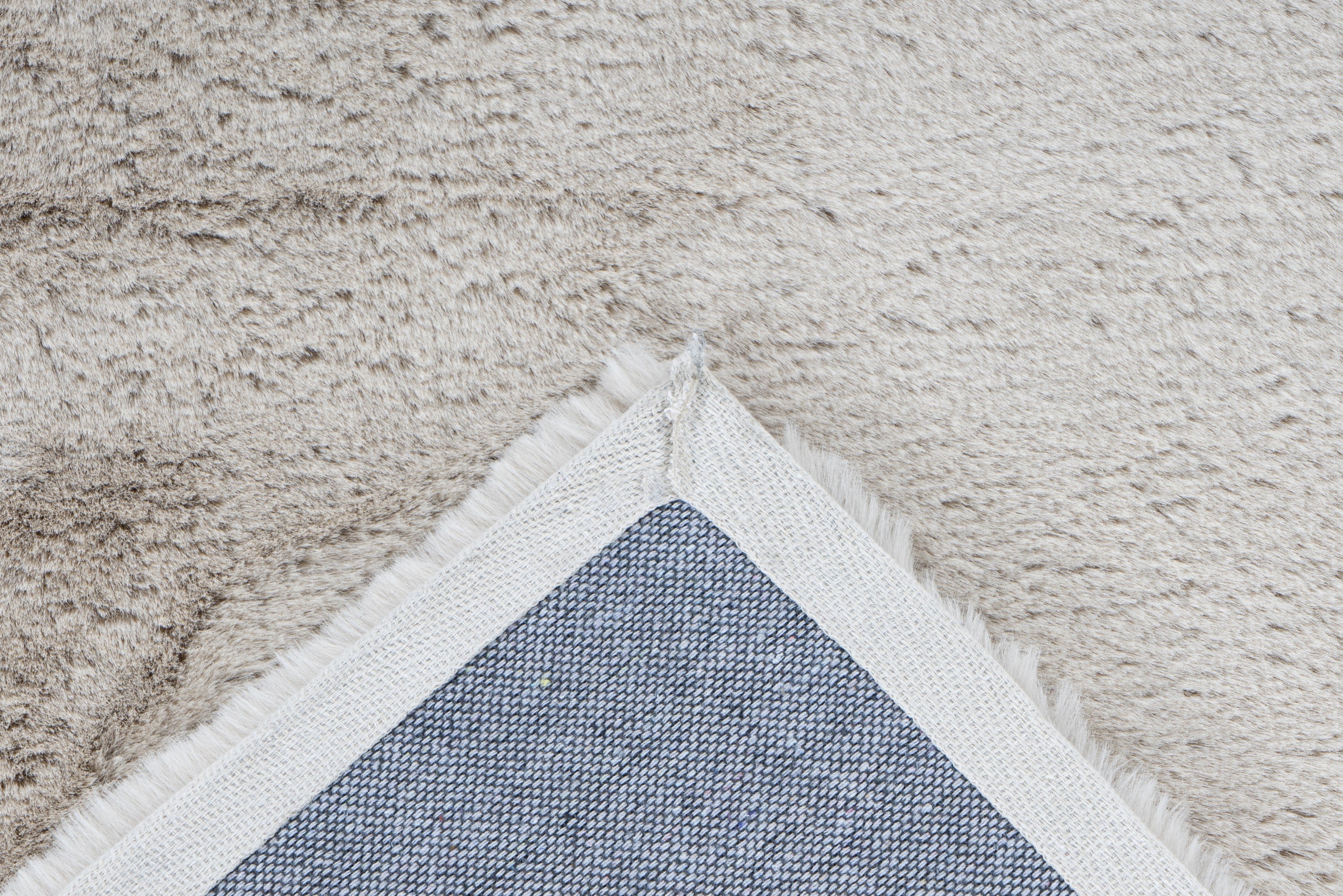 Detailshot van de onderzijde van het zandbeige Cloud vloerkleed, netjes afgewerkt