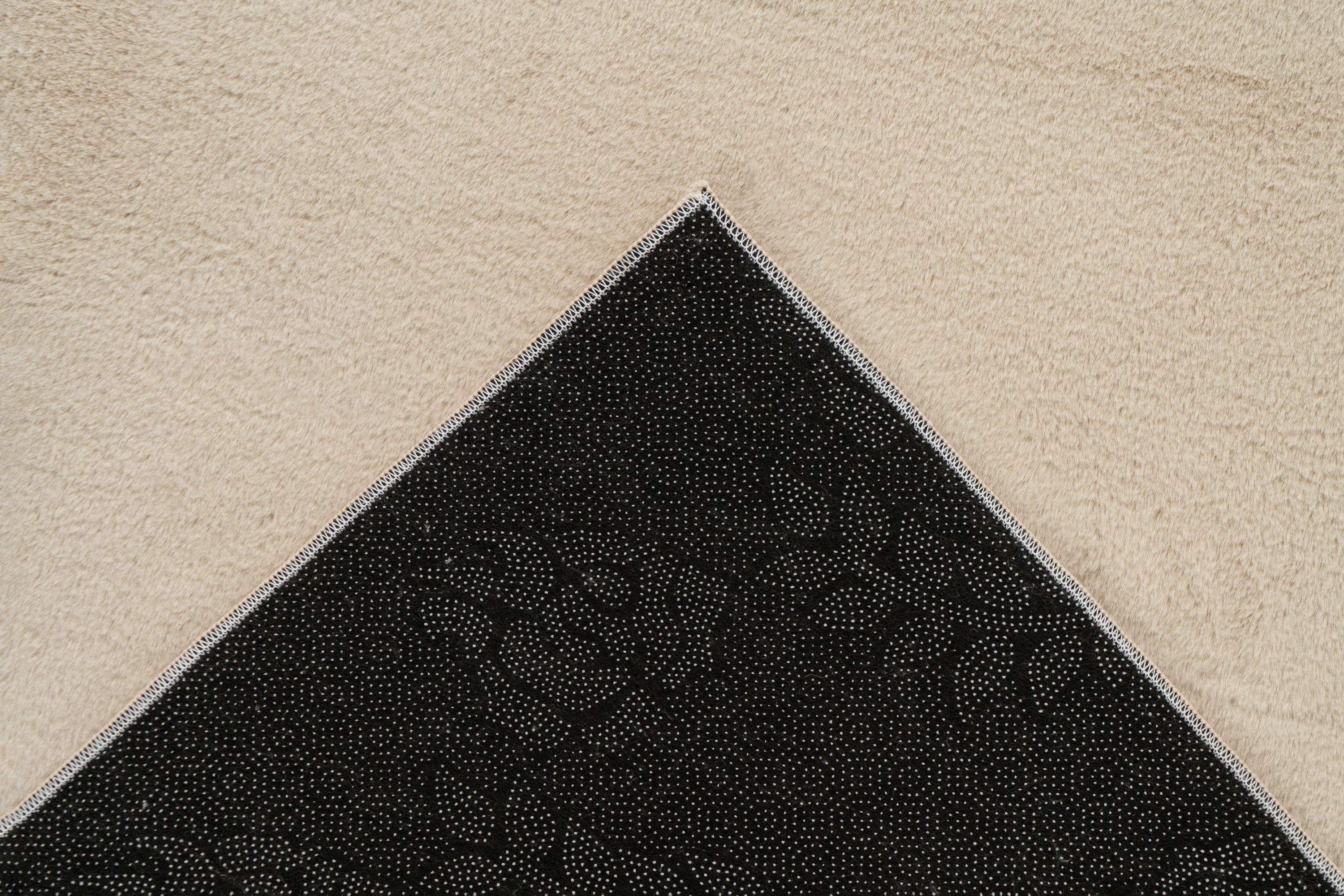 Ingezoomde hoek van beige Softcare vloerkleed met zicht op de backing