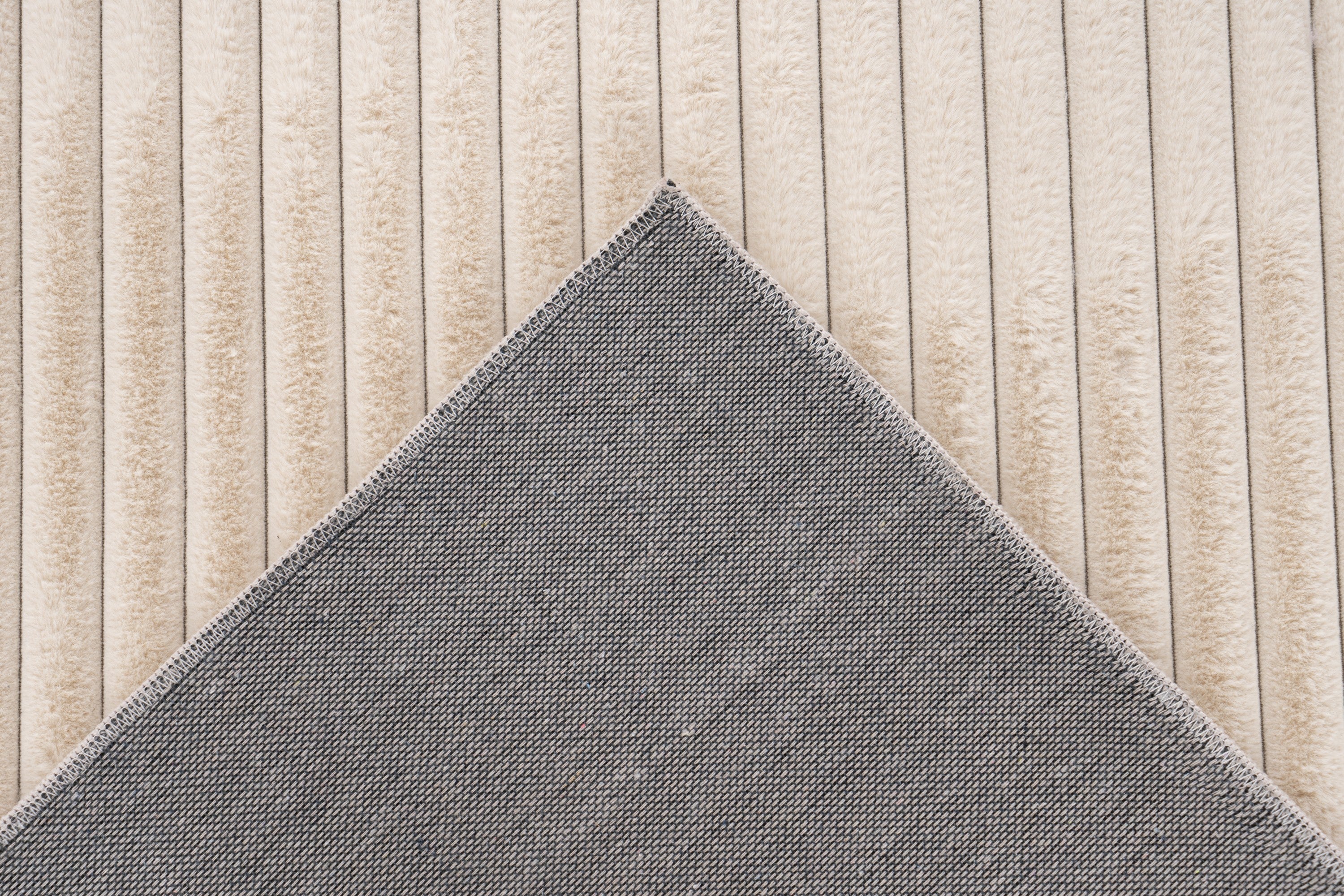 Close-up van een hoekje van het beige Lushlyn vloerkleed, waar je de backing goed kunt zien