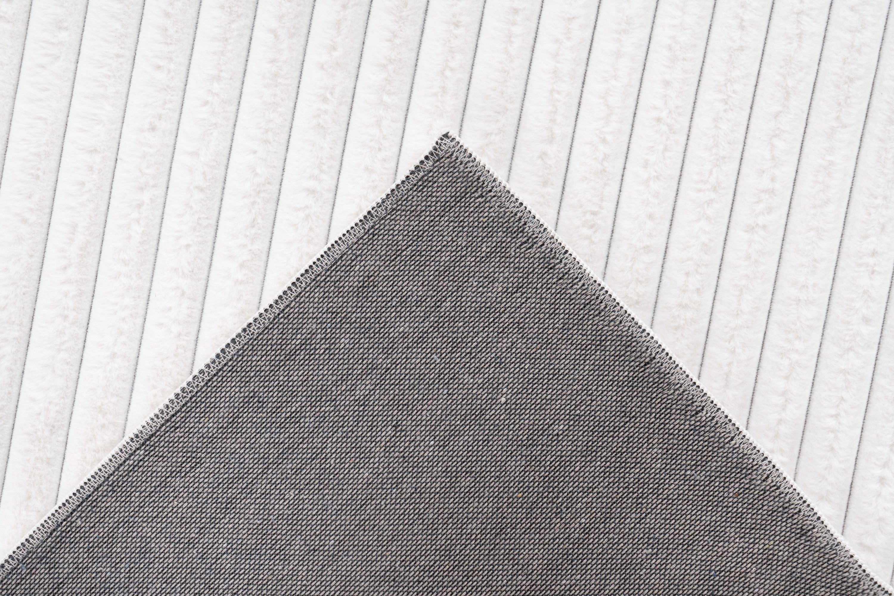 Close-up van een hoek van het witte Lushlyn vloerkleed met zicht op de backing