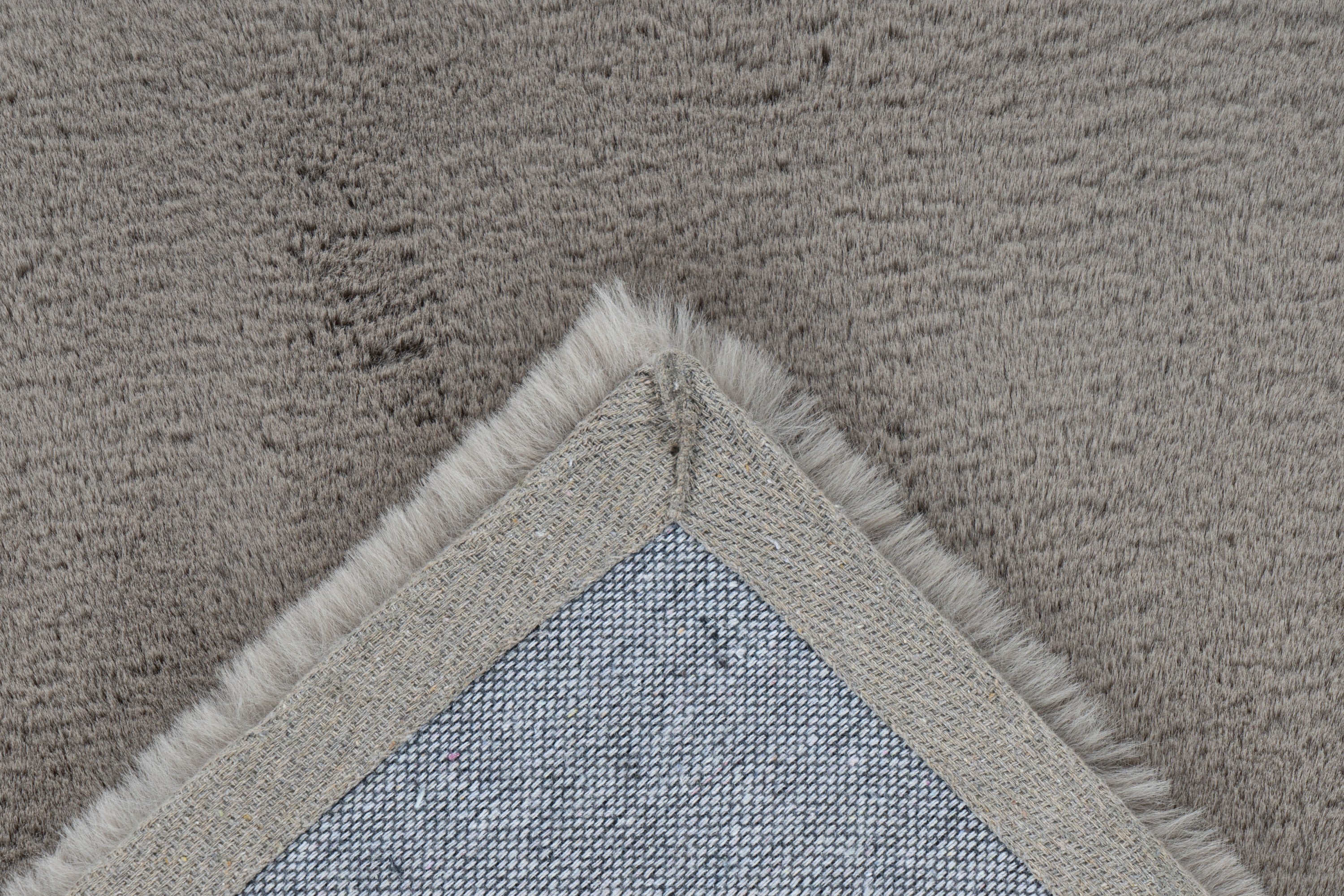 Close-up van een hoek van het taupe Vellyn vloerkleed met zicht op de backing
